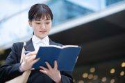 ビルの外で手帳を開きスケジュールを確認する学生